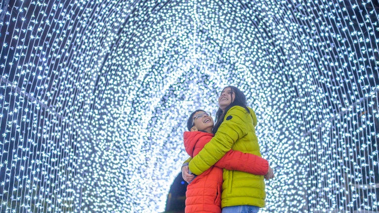 A young boy and girl embrace one another in a tunnel of blue fairy lights.